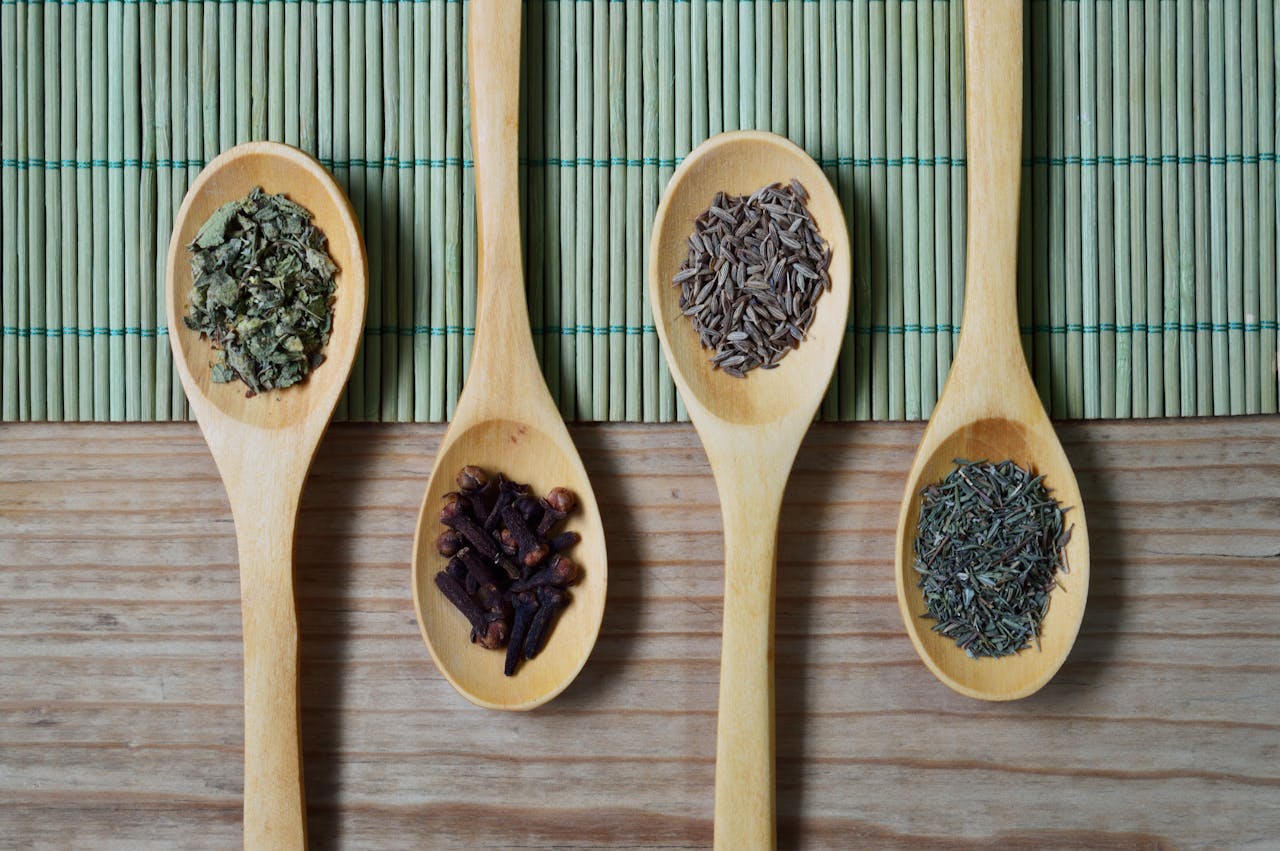 services-04 Overhead view of wooden spoons filled with spices and herbs on a bamboo mat, ideal for culinary themes.