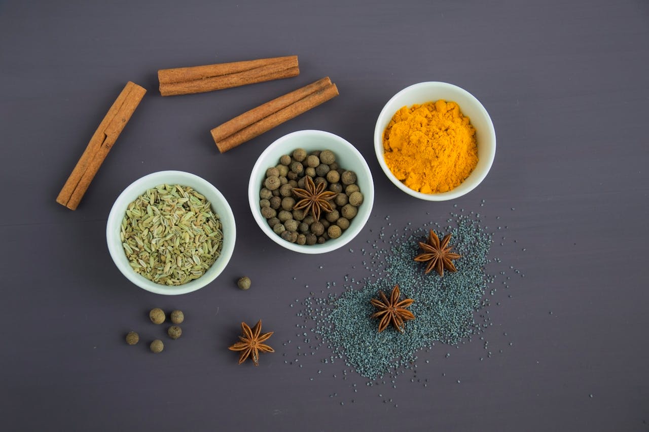 services-02 Flat lay of assorted spices including cinnamon, turmeric, and star anise on a dark surface.
